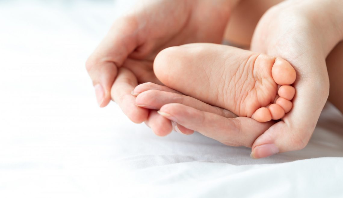 Stopa dziecka trzymana przez mamę, która regularnie stosuje krem do skóry i paznokci dla dzieci